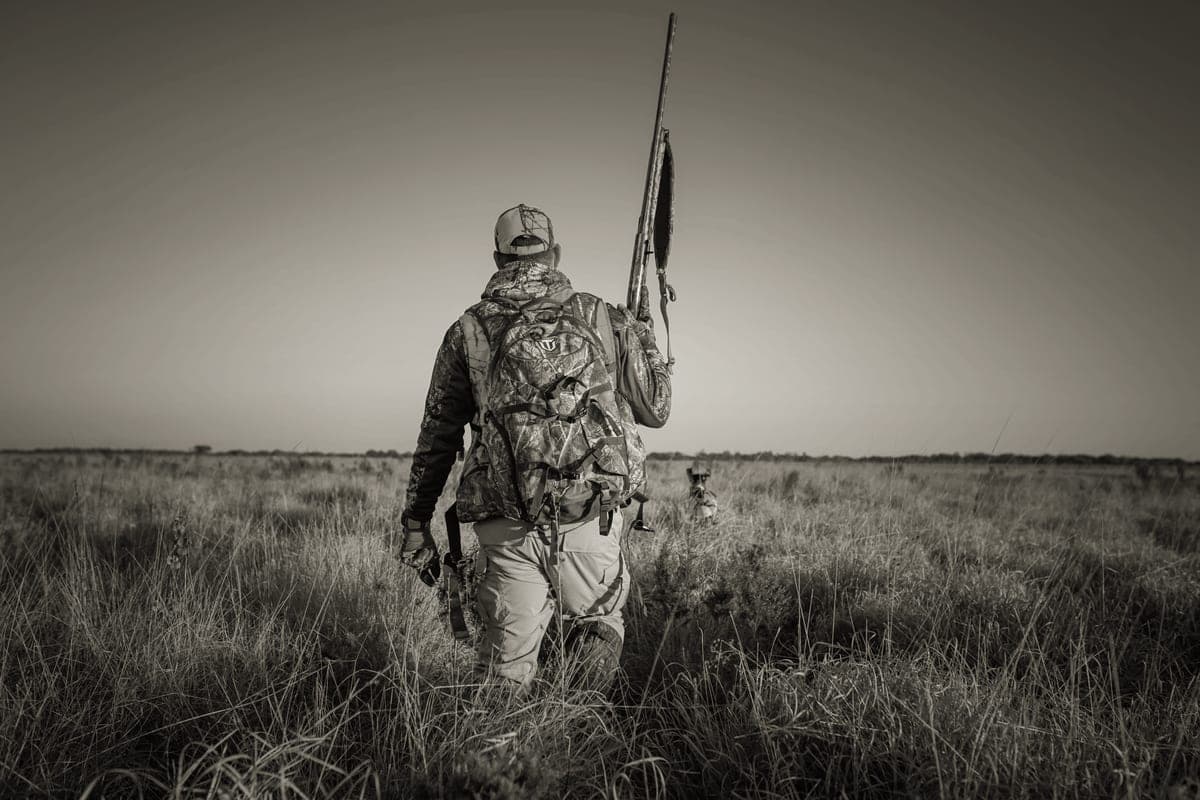 A hunter crossing an open field in low golden light